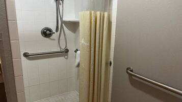 A bathroom with white tiled walls, a shower with a handheld showerhead, a towel rack, and a door with a metal handle.