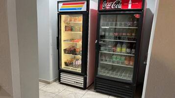 Two beverage vending machines, one with a colorful top and one with a red top, in a hallway.