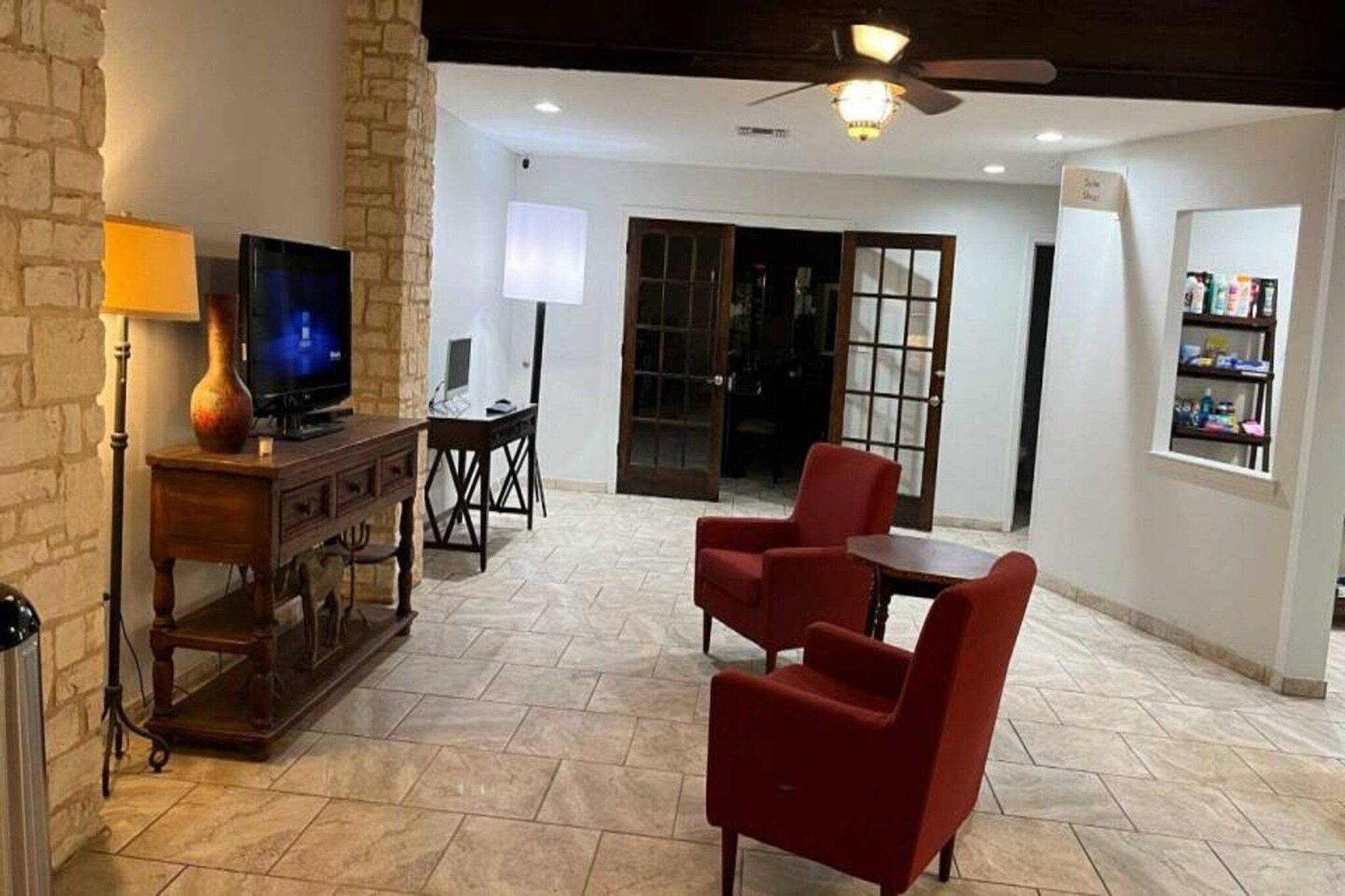 Uma sala de estar com televisão, luminária, lareira, uma poltrona vermelha, mesa e estante de livros.