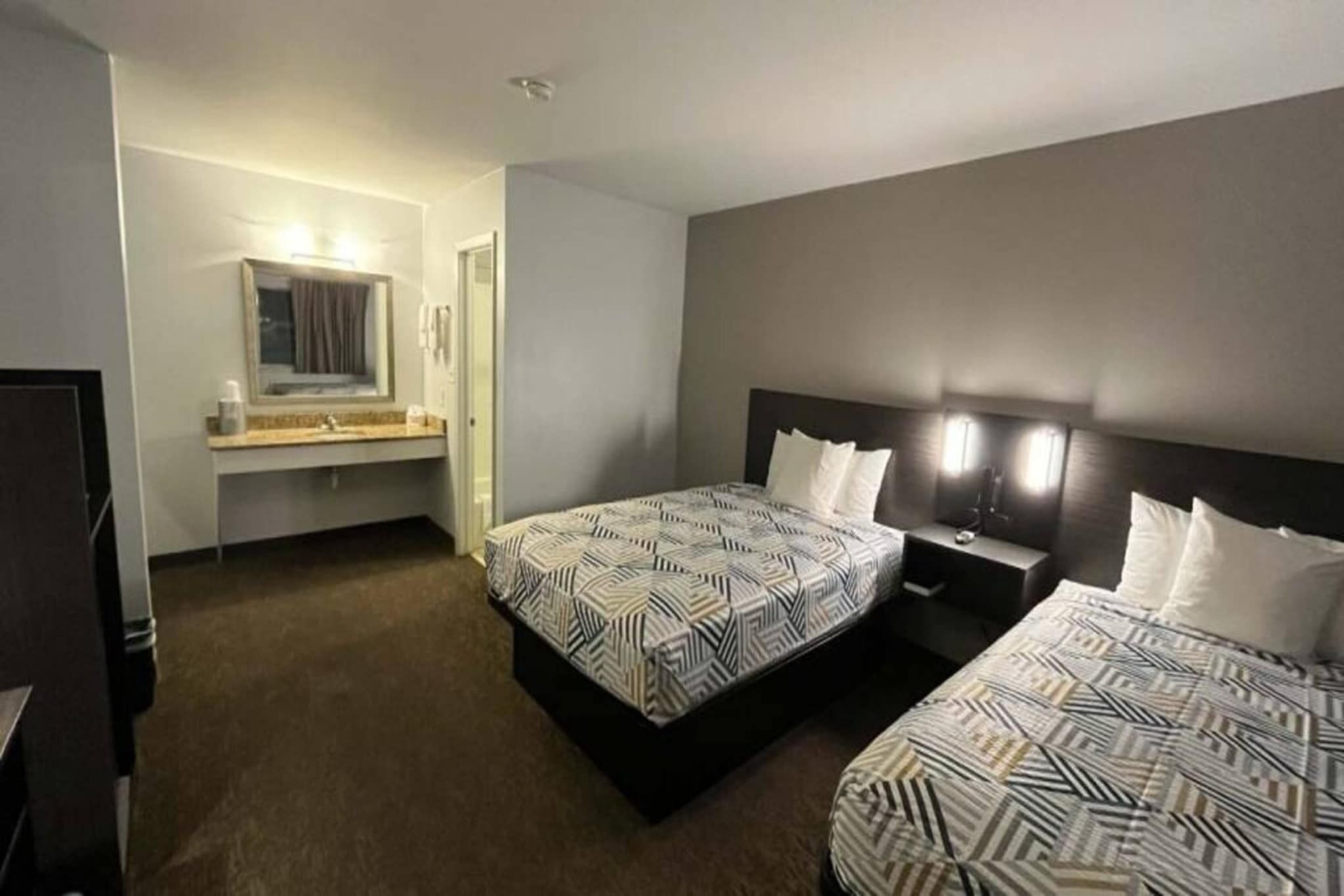 A hotel room with two beds, a bathroom, and a desk.