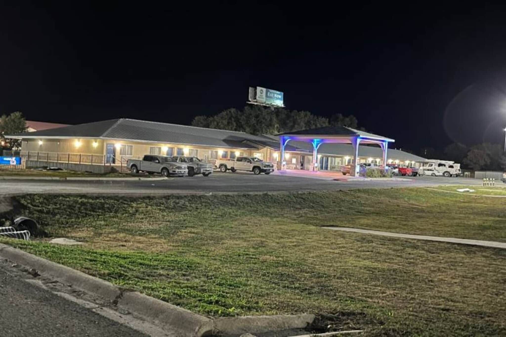 Een motel met een parkeerplaats, een overdekt buitengebied en een bord waarop 'Nu vertrekken' staat.