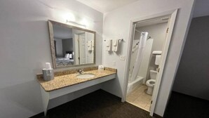 Une salle de bain avec un lavabo doté d’un plan de travail en granit, un grand miroir et un espace douche.