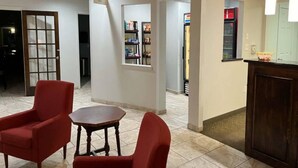 Un hall d’hôtel avec un comptoir d’accueil, une petite table ronde et deux fauteuils rouges.
