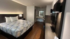 Une chambre d’hôtel avec un lit, un bureau, une télévision et une salle de bain que l’on aperçoit à l’arrière-plan.