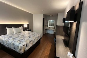 Quarto de hotel com cama, escrivaninha, televisão e banheiro ao fundo.