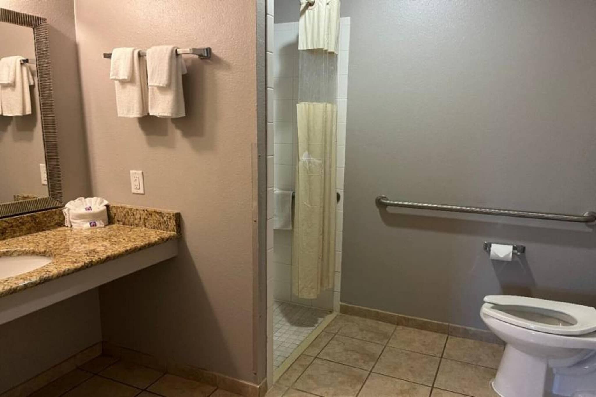 A bathroom with a granite countertop, a mirror, a towel rack, a shower with a glass door, and a toilet.