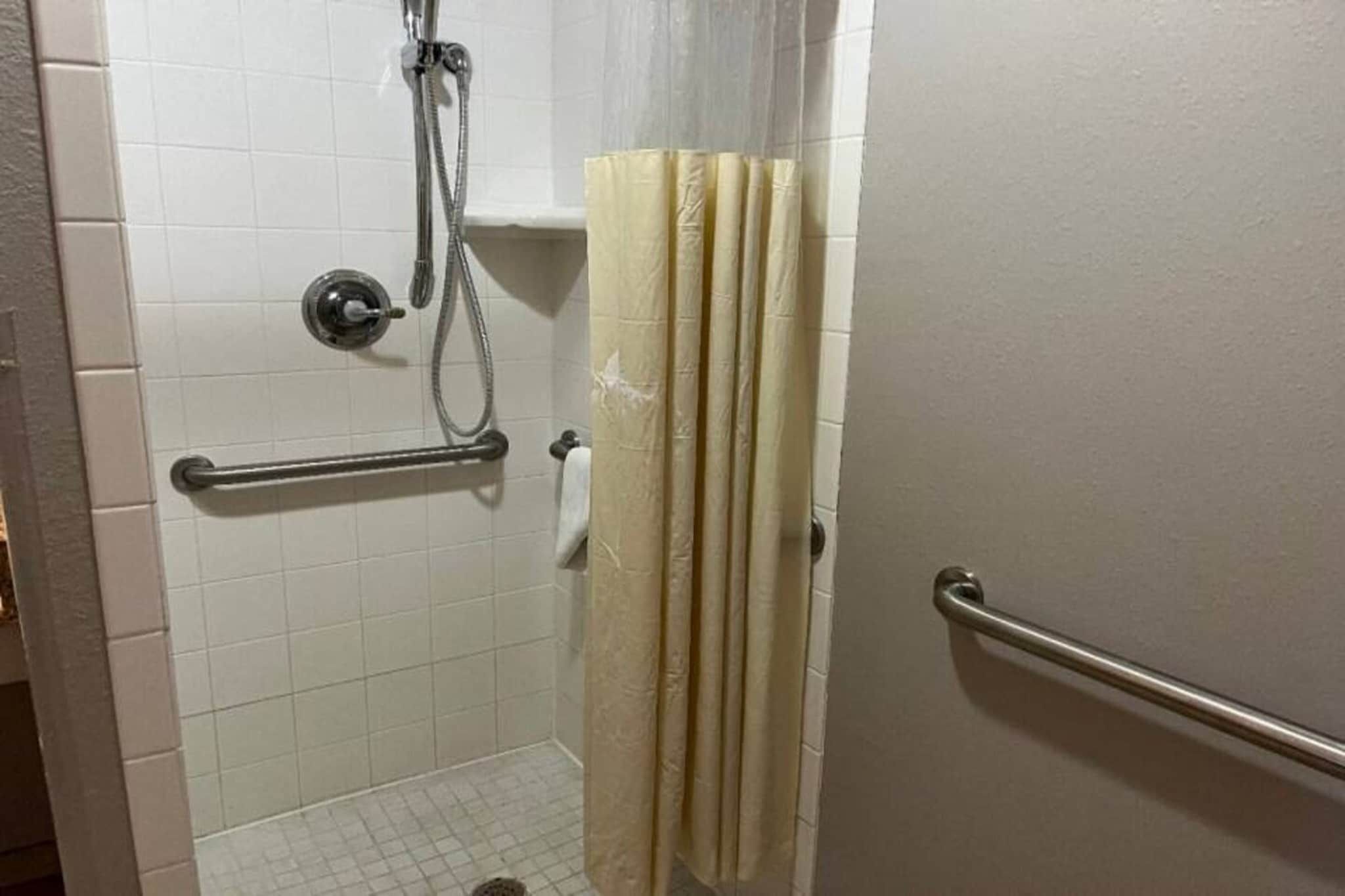A bathroom with white tiled walls, a shower with a handheld showerhead, a towel rack, and a door with a metal handle.