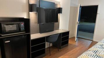 A compact room with a kitchenette, a flat-screen TV mounted on the wall, a single chair, and a bed with a patterned cover.
