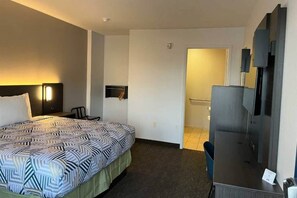 A hotel room with a bed, a desk, a chair, a TV, and a door leading to a bathroom.