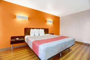 Une chambre d’hôtel avec un lit, une table de chevet et une lampe fixée au mur.