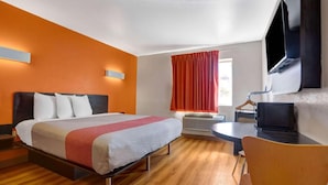 Hotellihuone, jossa on sänky, työpöytä, tuoli, televisio ja ikkuna, jossa on verhot.