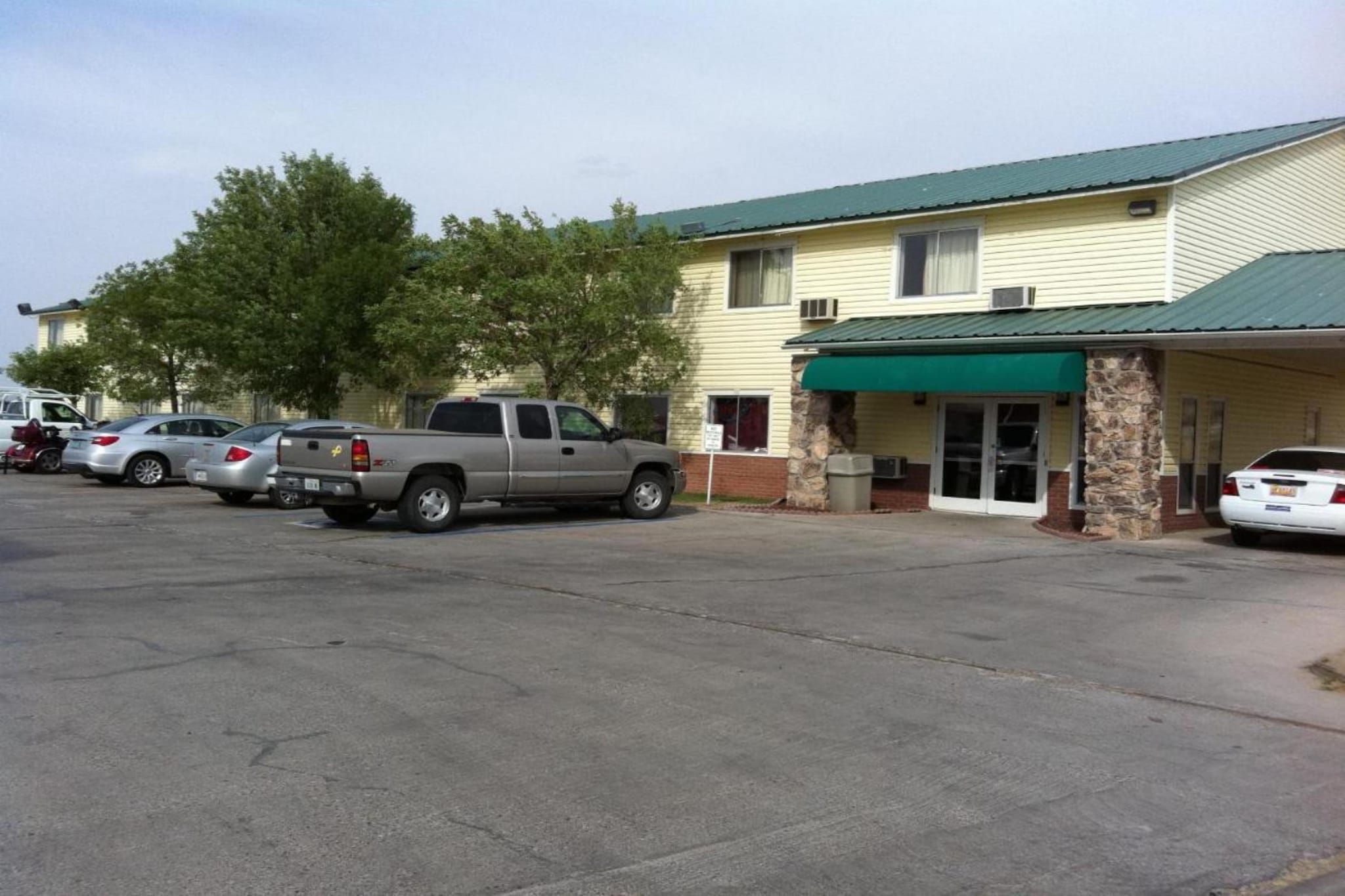 A building with a green awning, a parking lot with several cars, and a stone pillar.