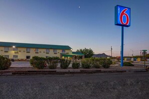 A motel with a large sign displaying the number 6, a parking lot, and a building with a green roof. - 2 Queen Beds | Non-Smoking (Truth or Consequences)