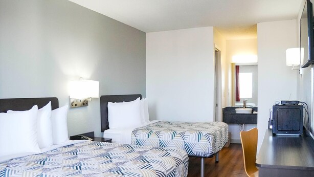 A hotel room with two beds, a desk, a chair, a TV, and a bathroom visible through an open door. - 2 Queen Beds|Nsmk,Micfridge (Rolla)