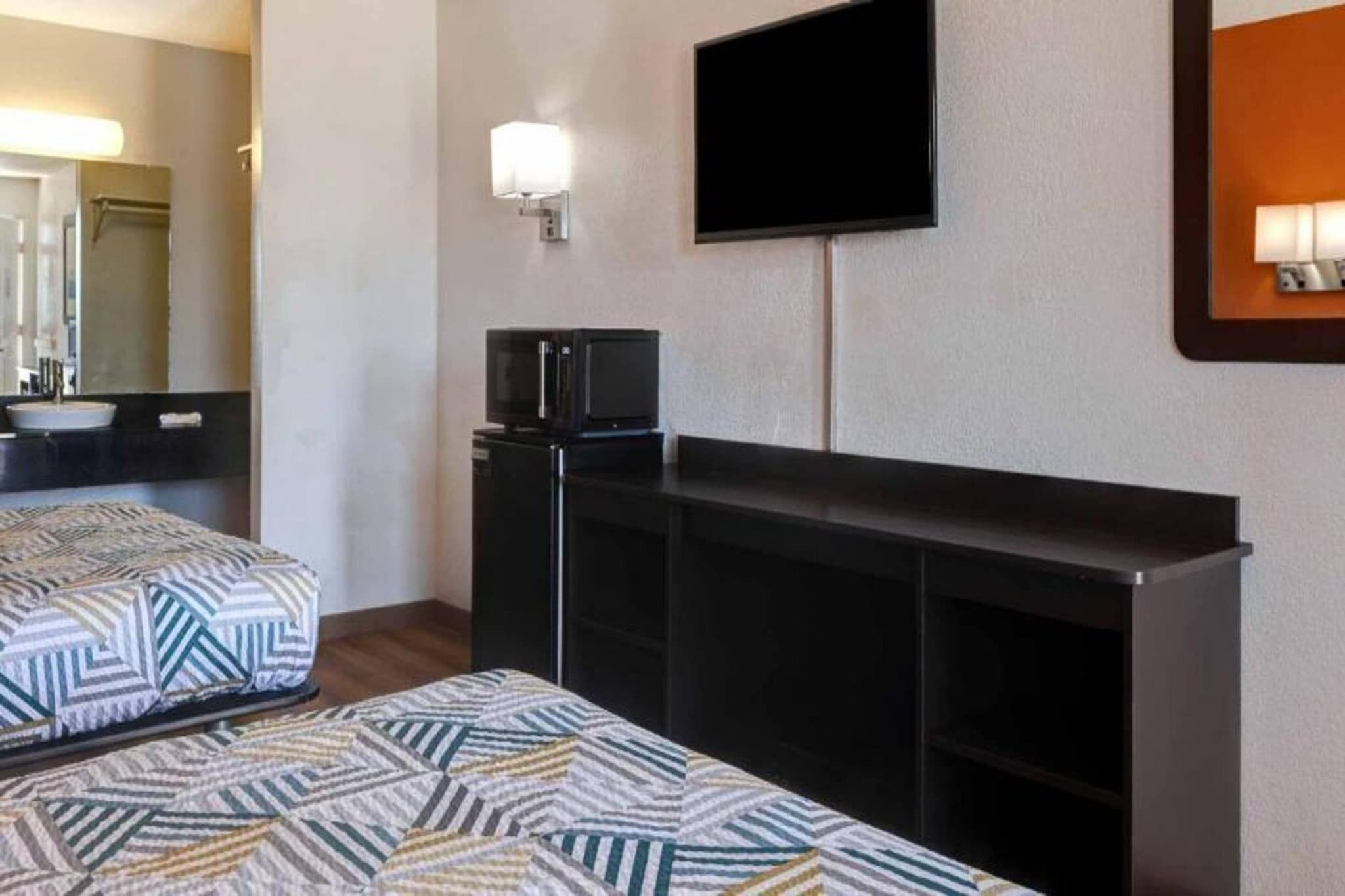 A hotel room with two beds, a TV mounted on the wall, and a small kitchenette area.