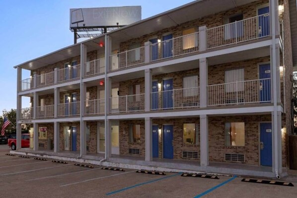 Un motel de varios pisos con fachada de ladrillo, balcones y estacionamiento.