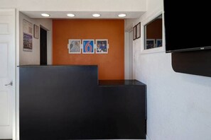Un espace d ’accueil avec un comptoir noir, un mur orange et des tableaux encadrés.