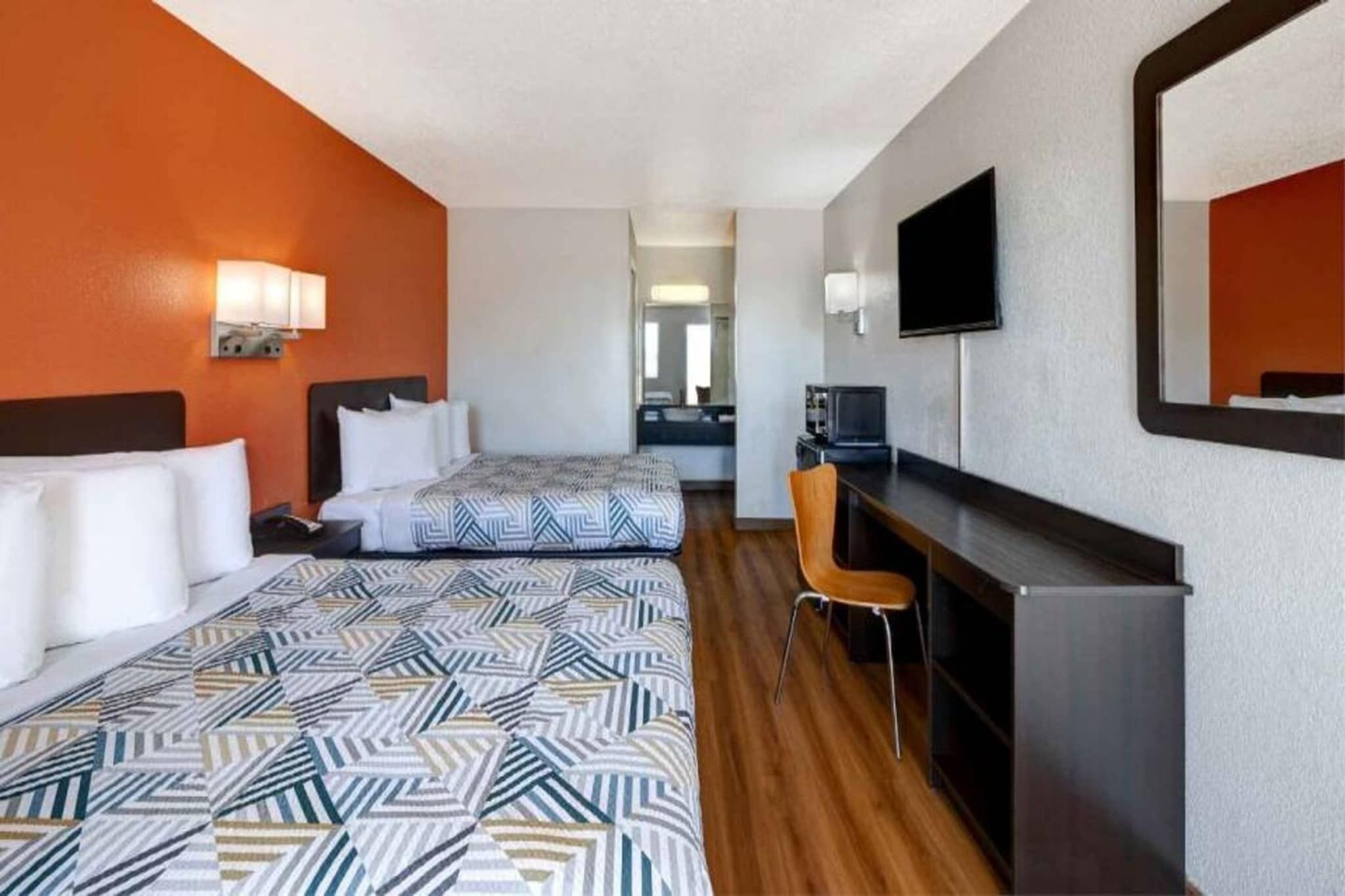 A hotel room with two beds, a desk, a chair, and a television.