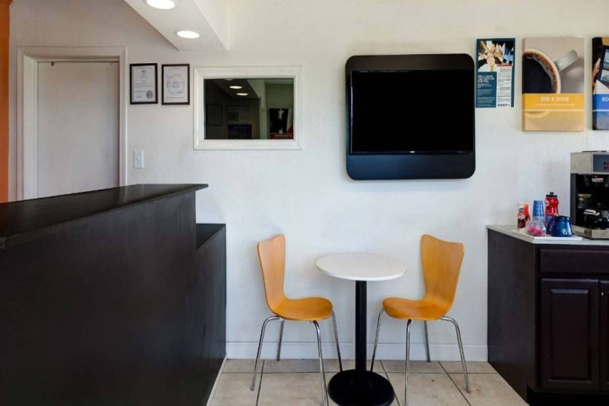 A reception area with a counter, two chairs, a small table, a flat-screen TV, and a coffee machine.
