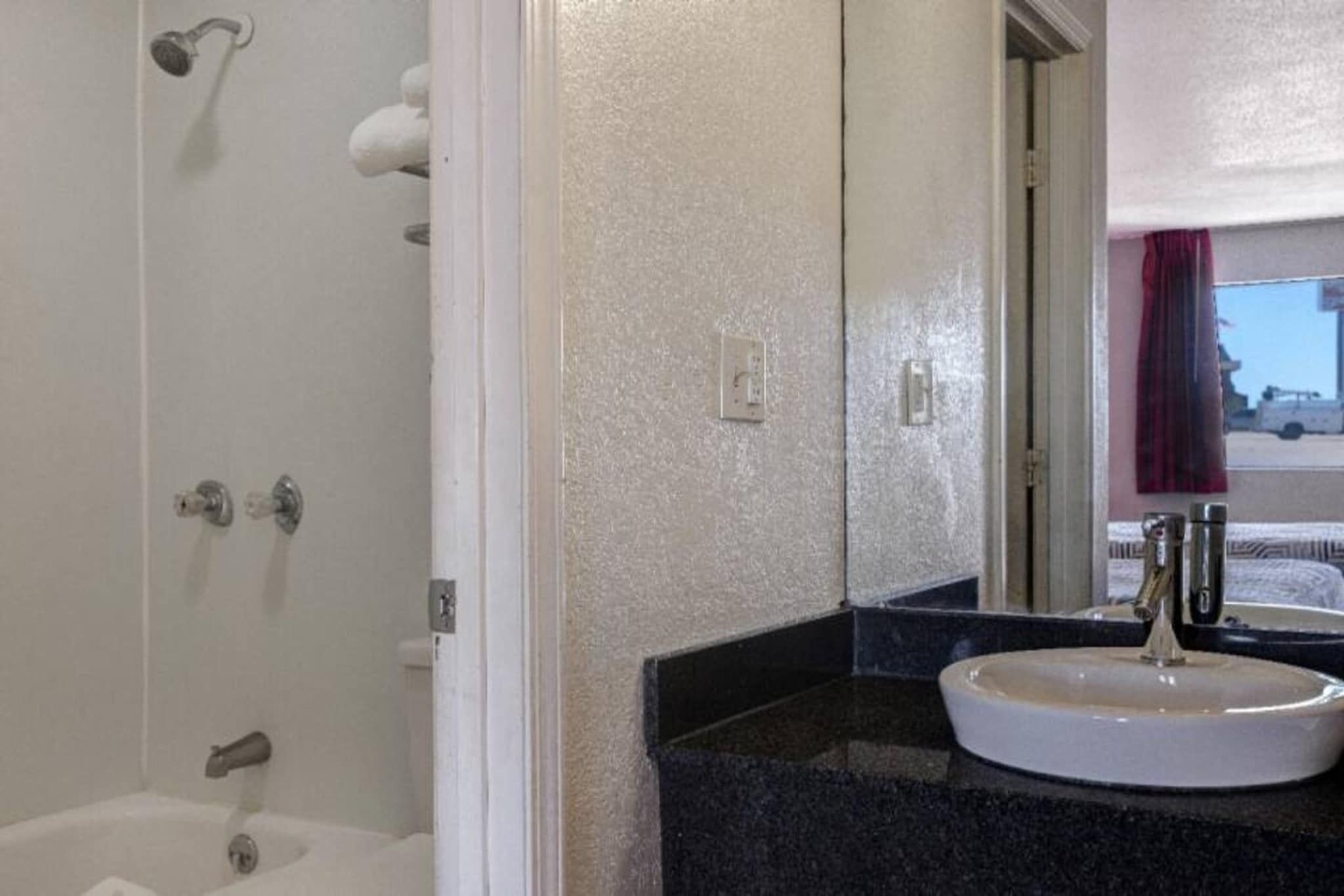 A bathroom with a white bathtub, a sink with a faucet, and a mirror reflecting a red curtain.