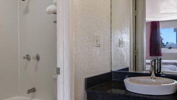 A bathroom with a white bathtub, a sink with a faucet, and a mirror reflecting a red curtain.