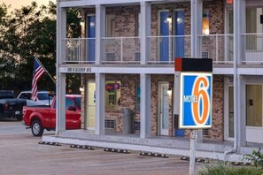 Motel con un letrero que indica el número 6, con una estructura de dos pisos y un balcón en el nivel superior.