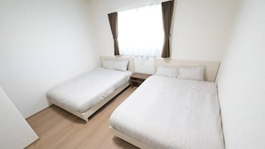 Ein Zimmer mit zwei Einzelbetten, einem kleinen Nachttisch und einem Fenster mit Vorhängen.