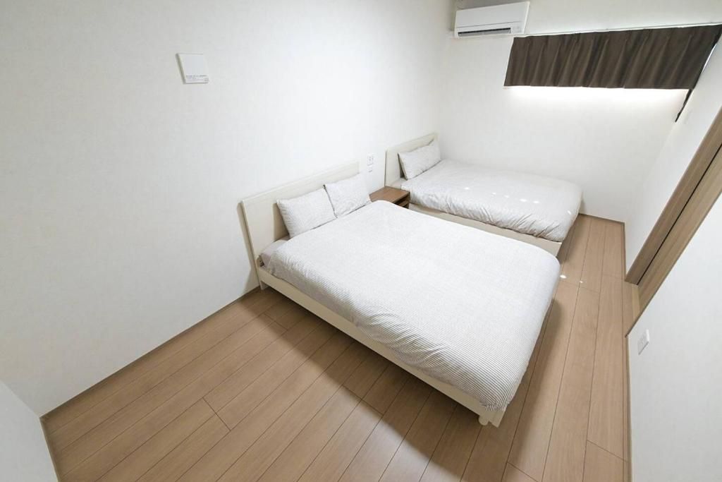 A room with two beds, a wooden floor, and an air conditioning unit.