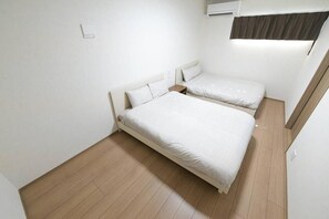 A room with two beds, a wooden floor, and an air conditioning unit. - LA CHIC Stay Ozu (kikuchigun/oozumachi/muro)