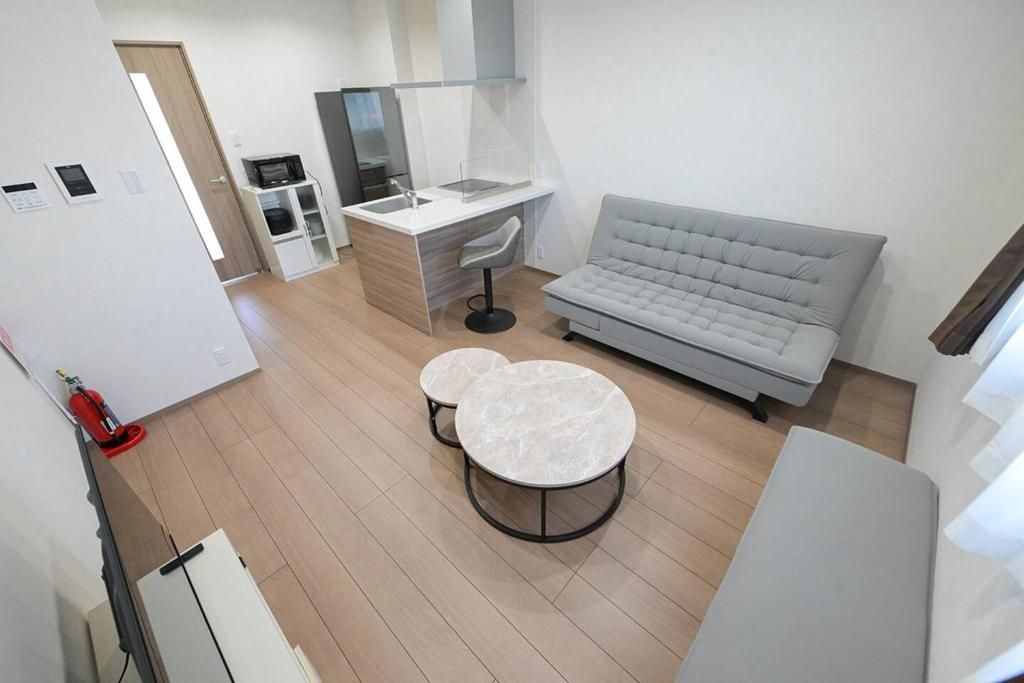 A modern kitchen with a built-in microwave, a dining area with two round tables, and a grey sofa.