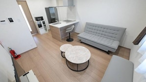 Eine moderne Küche mit integriertem Mikrowellenherd, ein Essbereich mit zwei runden Tischen und ein graues Sofa.