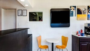 Een receptiegedeelte met een balie, twee stoelen, een televisie en een koffieapparaat.