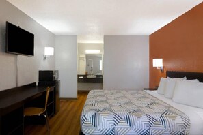 A hotel room with a bed, desk, chair, television, and a bathroom visible through an open door.