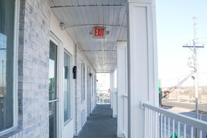 A covered outdoor corridor with a white brick wall, glass doors, and an exit sign. - 1 King Bed|Nsmk,Micfridge (Rolla)