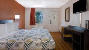 Een hotelkamer met een bed, een bureau, een stoel, een televisietoestel en een raam met gordijn.