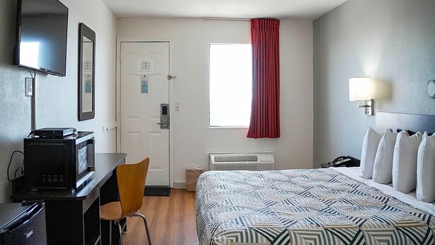 Een hotelkamer met een bed, een bureau met een televisie, een stoel, een raam met rood gordijn en een wandlamp.
