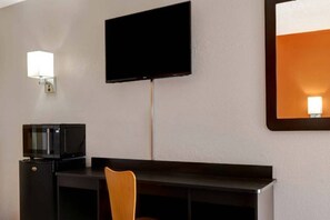 A hotel room with a flat-screen TV mounted on the wall, a small TV on a stand, a desk, and a chair.