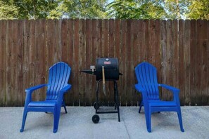 Two blue chairs and a grill in front of a wooden fence.