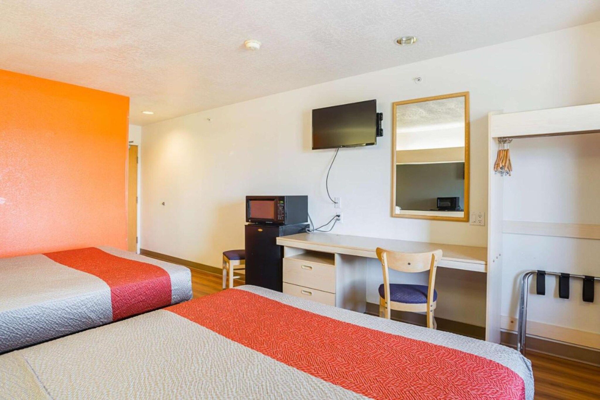 A hotel room with two beds, a desk with a chair, a television, a mirror, and a wardrobe.