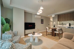 A modern living room with a flat-screen TV, a dining area with a round table, and a kitchen with a tiled backsplash. - Caruana, 2br, Peaceful, Modern (Istanbul)