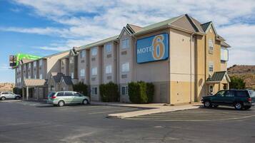 Un motel con un llamativo letrero de 'Motel 6', un estacionamiento y un edificio con múltiples ventanas y techo plano.