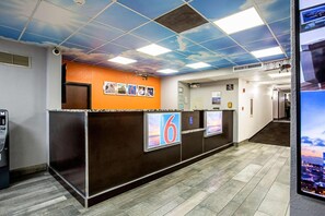 A hotel reception area with a modern design, featuring a reception desk, a digital screen displaying the number '6', and a corridor leading to other rooms. - Motel6 Atlanta|1 King Bed Non-Smoking (Atlanta)