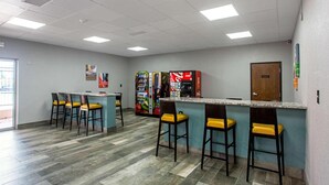 Zona de bar con mostrador y taburetes, máquinas expendedoras y una puerta.