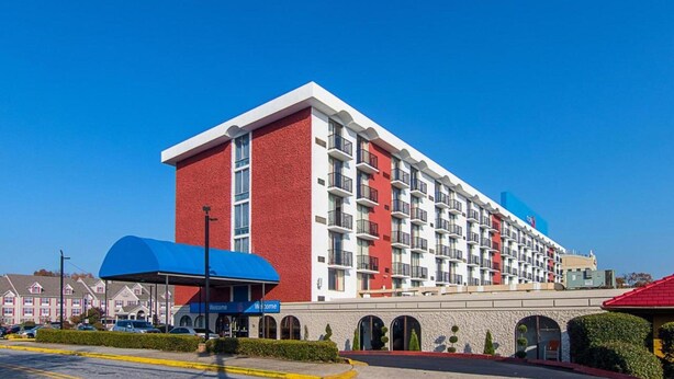 Un hotel de varios pisos con fachada roja y blanca, una entrada cubierta y un cielo azul despejado.
