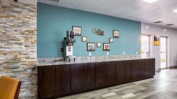 A reception area with a stone wall, a coffee machine, and framed coffee-related artwork on the wall.