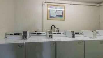 Une rangée de machines à laver de style industriel dans une buanderie, avec un mur blanc et un manuel d’instructions encadré.