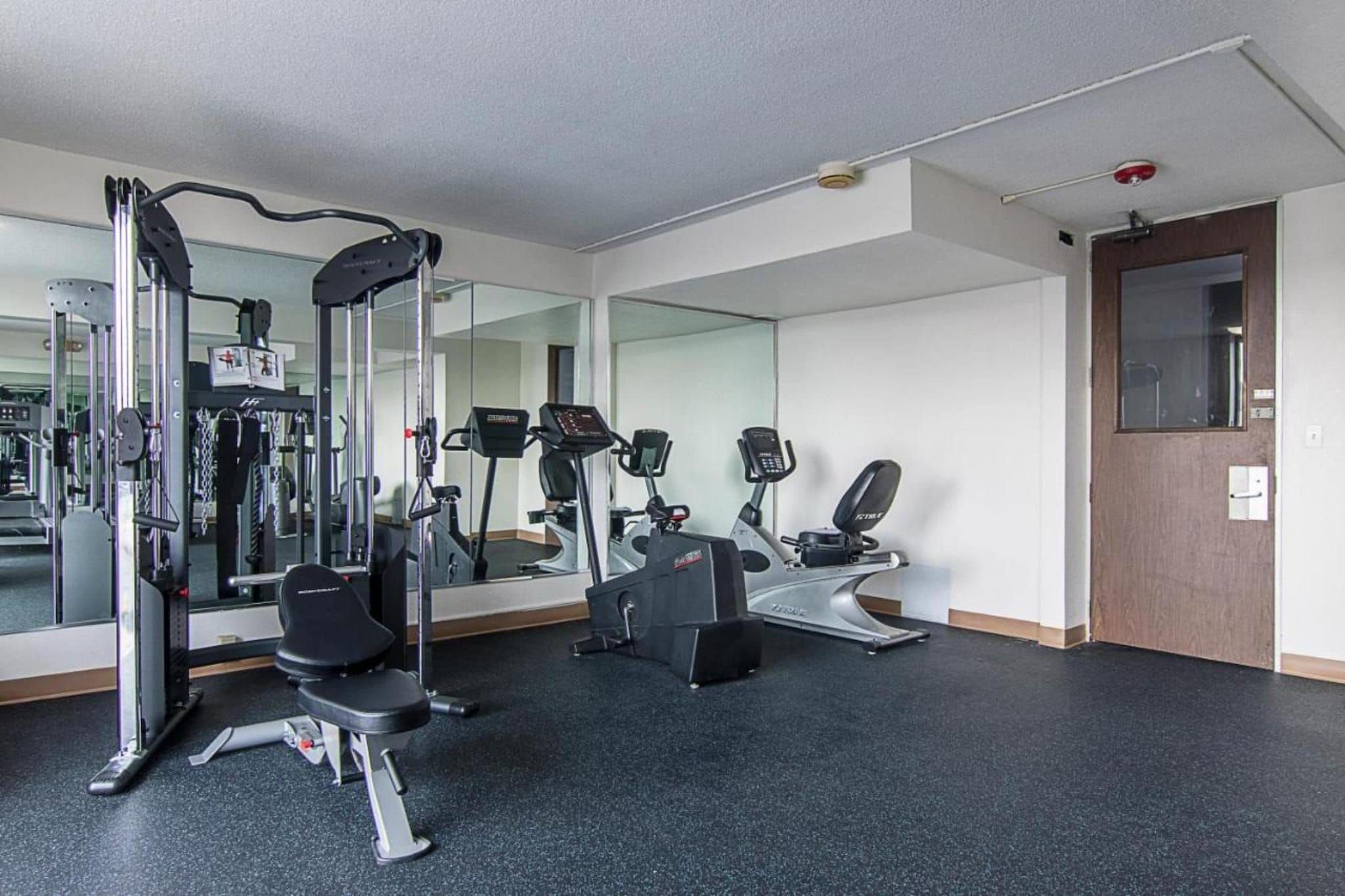 Ein Fitnessraum mit Trainingsgeräten, einem Spiegel und einer Tür.