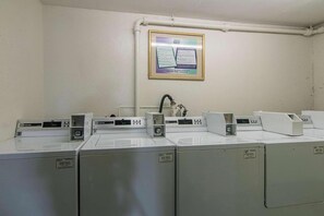 Eine Reihe von industriellen Waschmaschinen in einem Hauswirtschaftsraum mit weißer Wand und einem gerahmten Bedienungsanleitung.