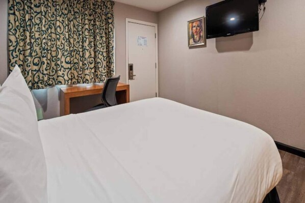 A hotel room with a bed, a desk, a chair, a television, and a door.