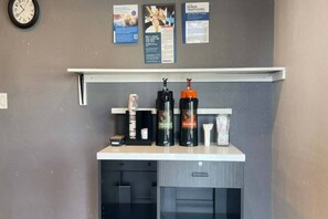 A kitchenette with a clock, a shelf with various items, and informational posters on the wall.